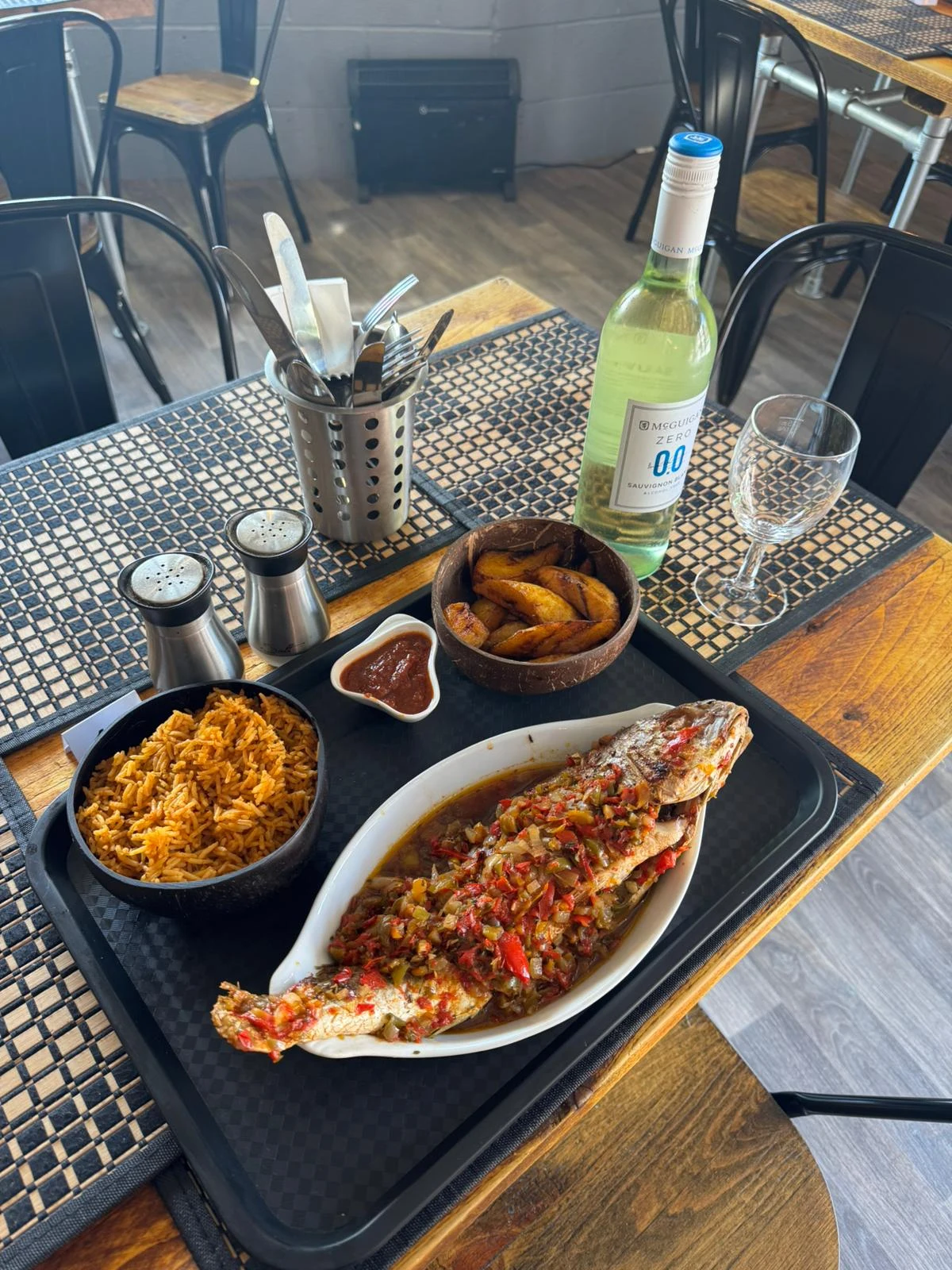 Whole croaker fish topped with peppers, with jollof rice, fried plantain and sauce.